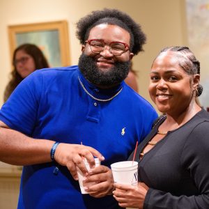 Two people smiling while holding white cups with red straws at a casual gathering.