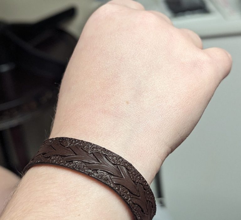 Close-up of a wrist wearing a dark brown braided leather bracelet, with a blurred background.